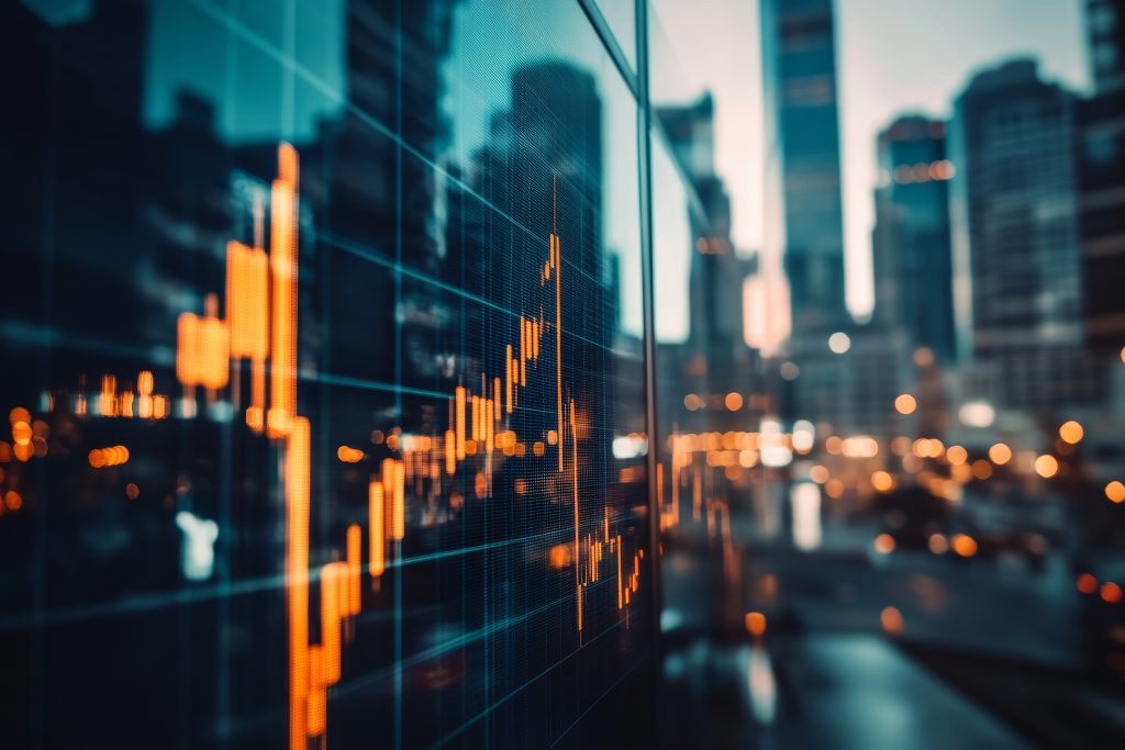 (Descrição da imagem: A imagem mostra uma sobreposição de um gráfico financeiro digital sobre a paisagem de uma cidade. Em primeiro plano e à esquerda, um gráfico de cotações do mercado financeiro, do tipo